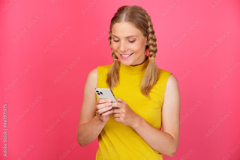 Portrait of a cheerful smiling young girl in yellow clothes standing isolated over pink background and using mobile phone Portrait of a cheerful smiling young girl in yellow clothes standing isolated over pink background and using mobile phone