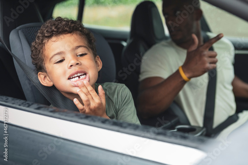 Playful boy showing broken teeth while sitting by father in electric car