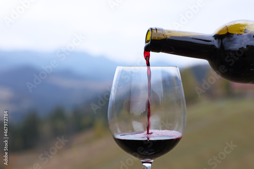 Pouring red wine into glass in mountains, closeup