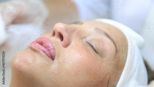 Facial peeling mask, spa beauty treatment, skin care. Woman getting facial treatment by beauty at spa salon, side view close up. Beautiful woman getting face massage in beauty spa. handheld shooting 