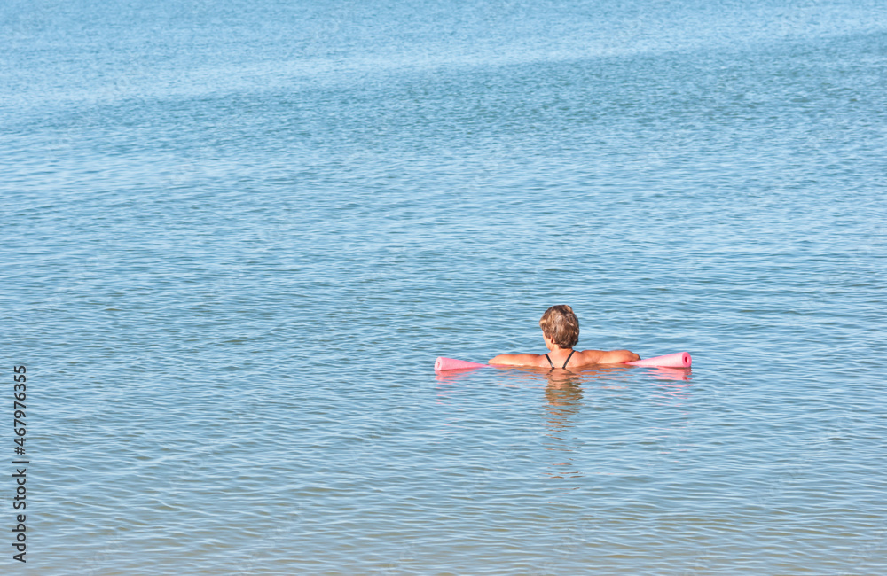 back view, far distance, of a middle aged female, resting on a pink float, in calm, tropical water, on sunny morning
