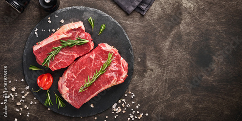 Fotografie Two raw steak New York  with rosemary and spices on a piece of parchment paper on old dark stone background