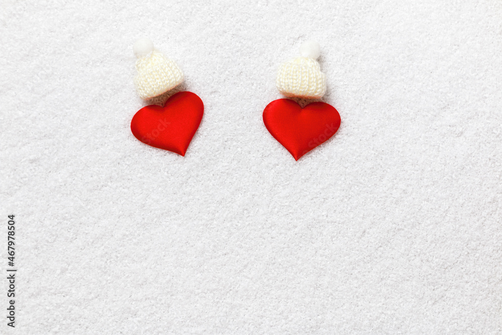 Fototapeta premium Two red hearts in white knitted hats on the snow.