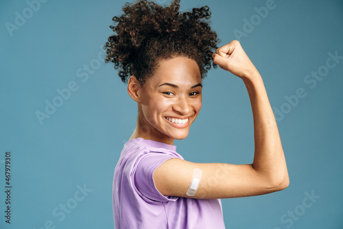 Happy young woman looking at camera, smiling and showing arm after vaccine injection