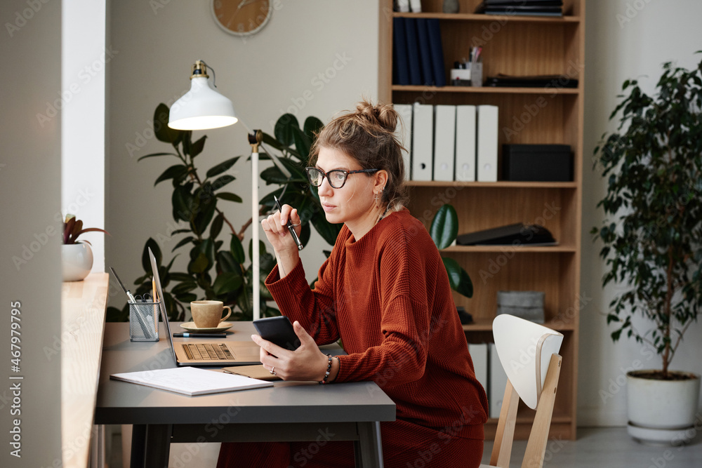 Young woman sitting at the table with laptop and using mobile phone at her work at office Young woman sitting at the table with laptop and using mobile phone at her work at office