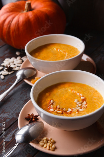 Two bowls of pumpkin soup with fresh pumpkin on dark wooden background