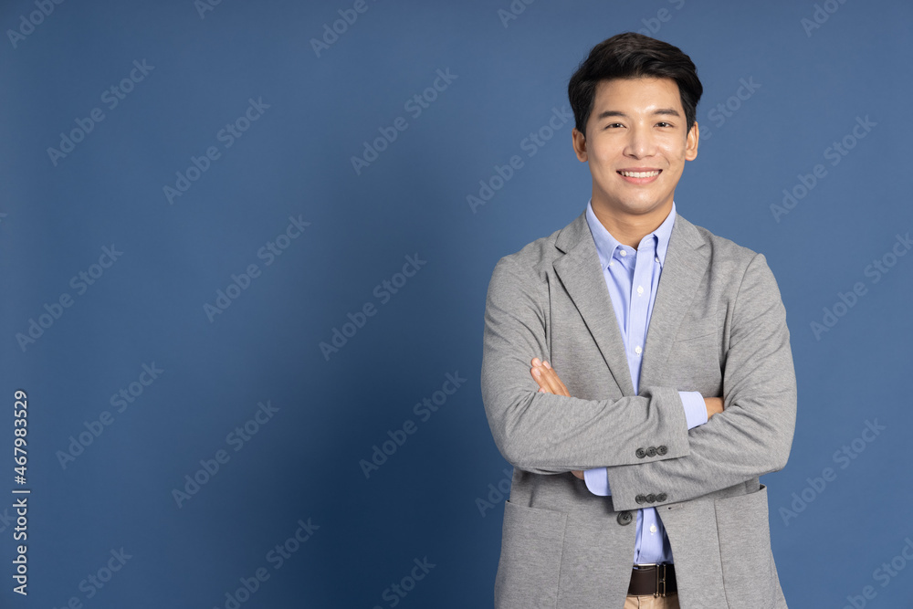 Smiling young Asian businessman with arms crossed in blue studio isolated background Smiling young Asian businessman with arms crossed in blue studio isolated background