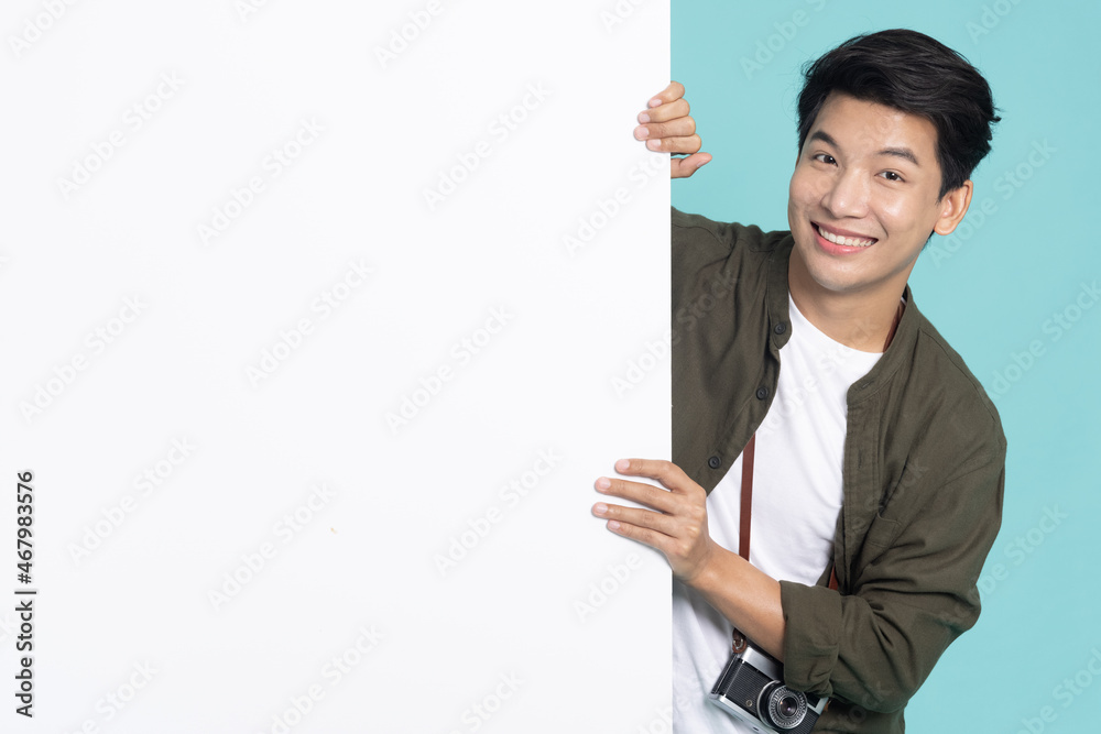 Young Asian man is standing behind the white blank banner or empty copy space advertisement board on green background, Looking at camera Young Asian man is standing behind the white blank banner or empty copy space advertisement board on green background, Looking at camera