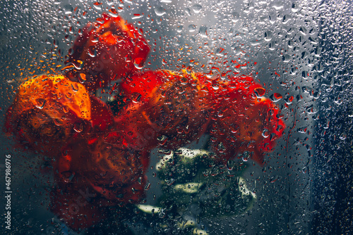 Bunch of beautiful faded flowers through the glass with rain drops