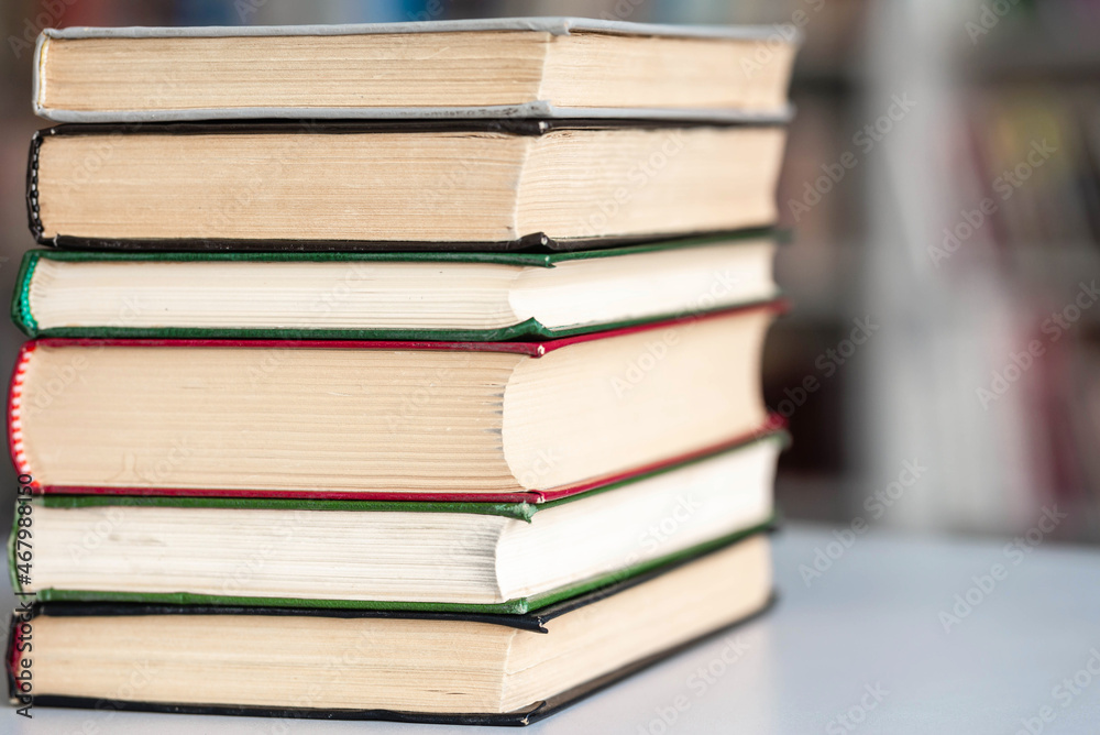 Books stack on wooden table and blurred bookshelf in library hall Books stack on wooden table and blurred bookshelf in library hall