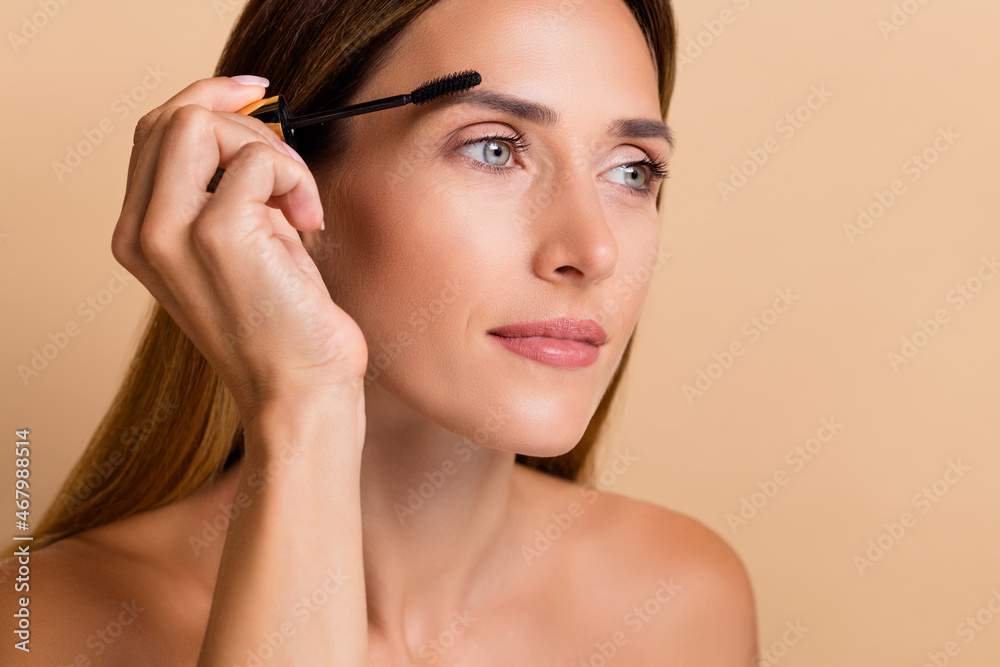 Cropped view portrait of attractive woman applying dying black eyebrow glamour isolated on beige pastel color background