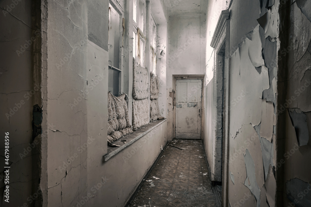 Corridor with windows in an old abandoned building. Dirty and shabby walls. The door is at the end of the hallway. Sunlight shines through the windows.