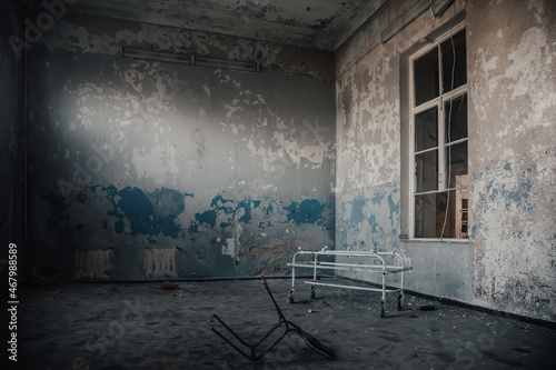 An old room with shabby walls in an abandoned building. Hospital gurney in the room. A ray of light on a shabby wall. Old broken window.