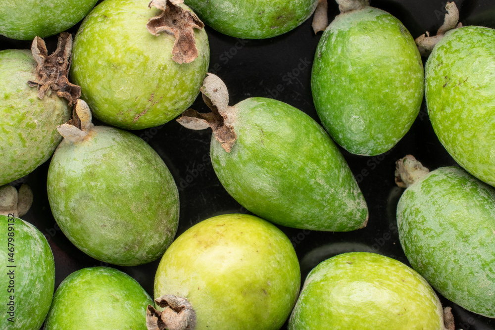 Several fragrant sweet feijoa fruits in a black bowl, close-up, top view. Several fragrant sweet feijoa fruits in a black bowl, close-up, top view.