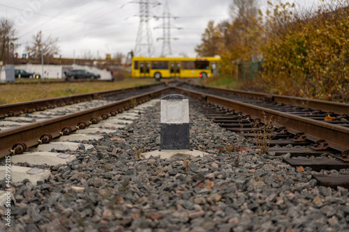 Photo of railway tracks connected at one distant point. Bus in the background. Railroad pole marker.