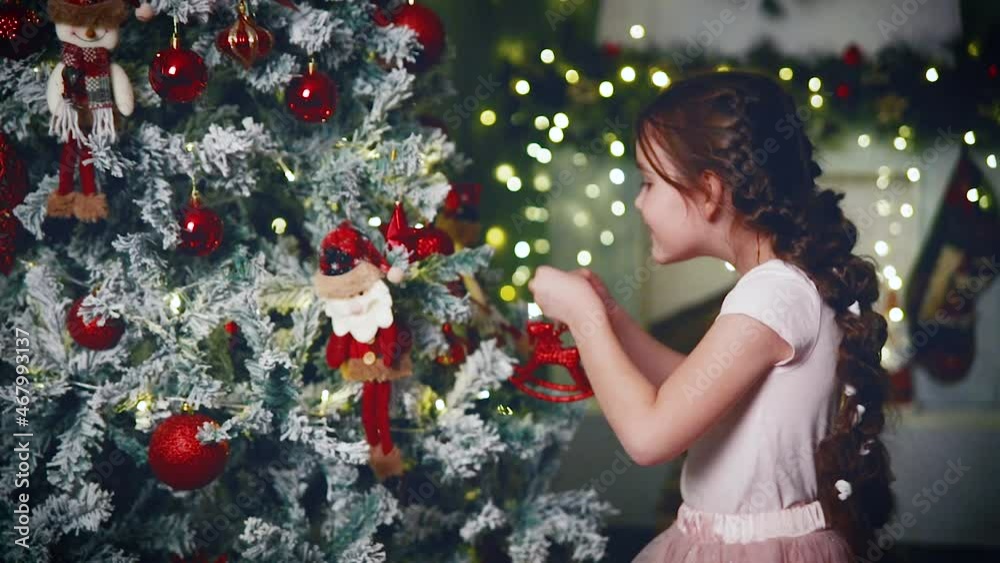A girl decorates a Christmas tree with toys. A girl decorates a Christmas tree with toys.