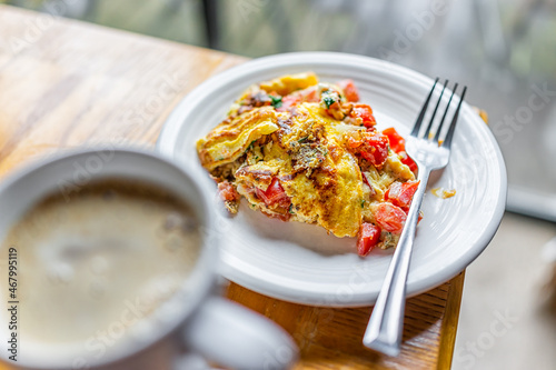 Homemade plate with cooked omelette amde with tomatoes, cilantro and red peppers vegetables on wooden kitchen table with fork, cup of coffee drink in mug photo