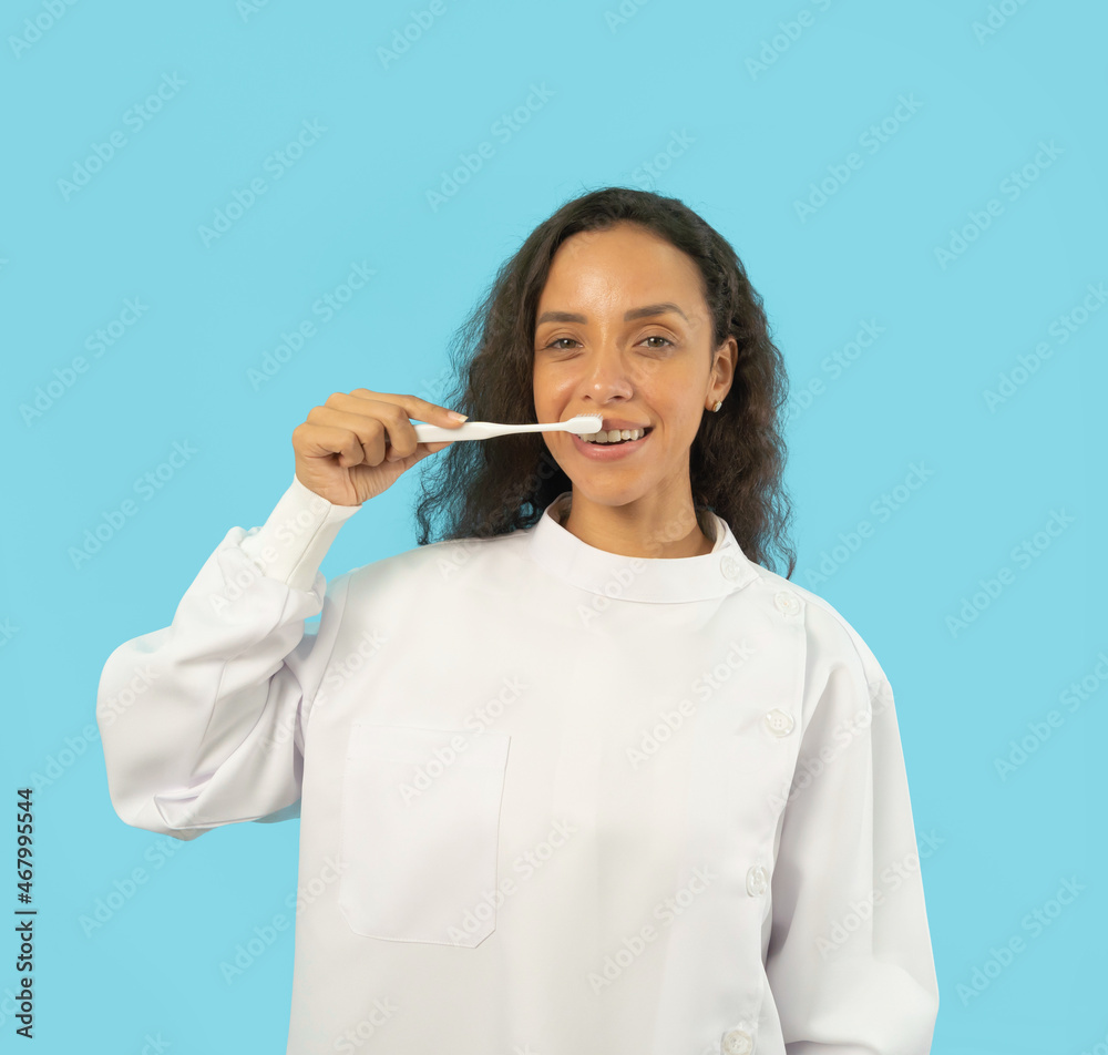 Portrait of happy Latin dentist woman, people smiling, brushing her teeth at hospital clinic. Doctor isolated on blue. Dentistry. Medical and dental health. Portrait of happy Latin dentist woman, people smiling, brushing her teeth at hospital clinic. Doctor isolated on blue. Dentistry. Medical and dental health.