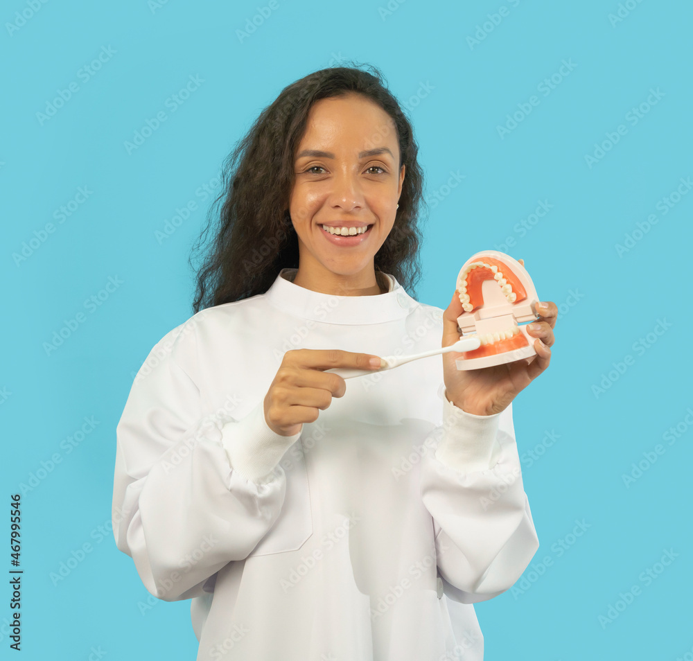 Portrait of happy Latin dentist woman, people smiling, holding denture teeth at hospital clinic. Doctor isolated on blue. Dentistry. Medical and dental health. Portrait of happy Latin dentist woman, people smiling, holding denture teeth at hospital clinic. Doctor isolated on blue. Dentistry. Medical and dental health.