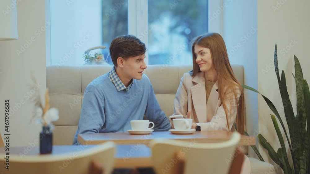Young man and woman having romantic date in cafe. Tracking shot sweethearts talking and looking at photos on her smartphone. Concept of relationship Young man and woman having romantic date in cafe. Tracking shot sweethearts talking and looking at photos on her smartphone. Concept of relationship