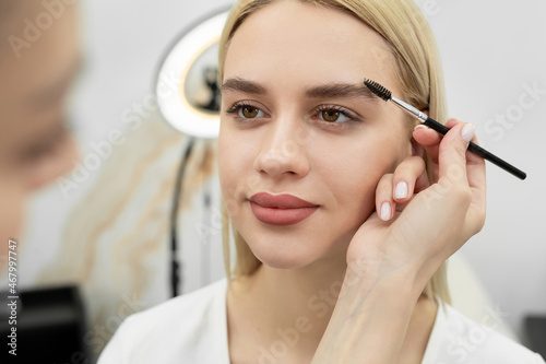 Closeup beautiful woman with eyebrow brush tool, makeup artist combs eyebrows close up.