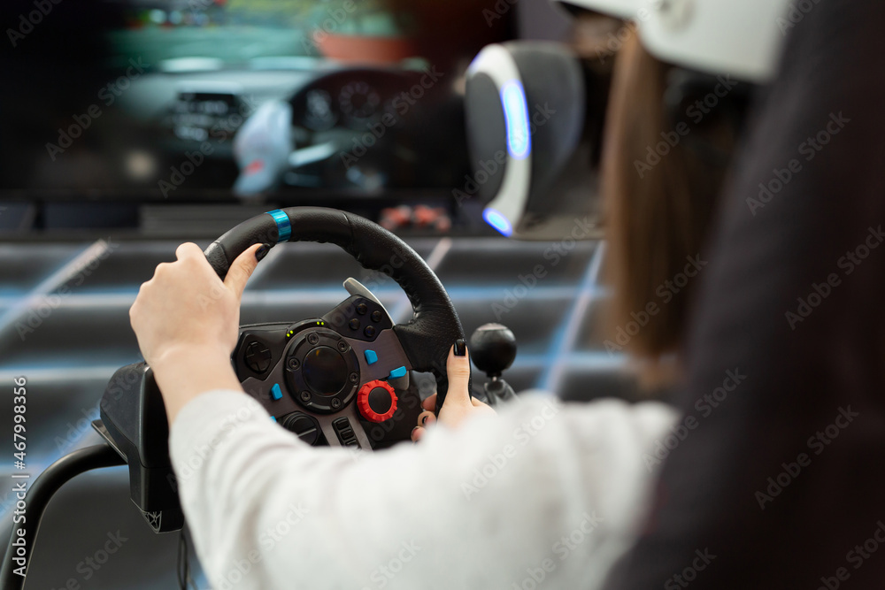 Close-up of the hands of a teenage girl in virtual reality glasses, who is holding the steering wheel and playing a computer game on the console.