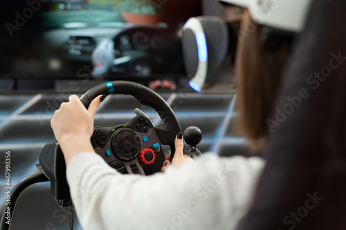 Close-up of the hands of a teenage girl in virtual reality glasses, who is holding the steering wheel and playing a computer game on the console. photo