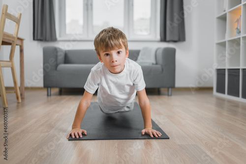 Boy-child doing classic push-ups at home in guest house on the floor on a sports mat.