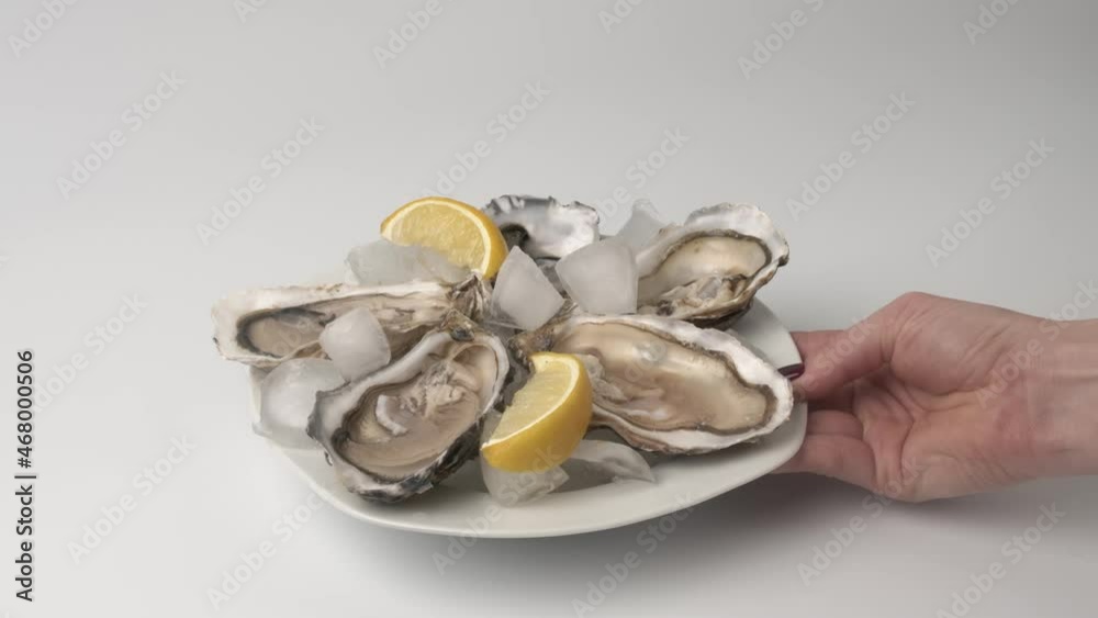 Oysters on ice with lemon closeup. Fresh Oyster on half shell on big plate in restaurant. Served table. 4K UHD video slow motion Oysters on ice with lemon closeup. Fresh Oyster on half shell on big plate in restaurant. Served table. 4K UHD video slow motion