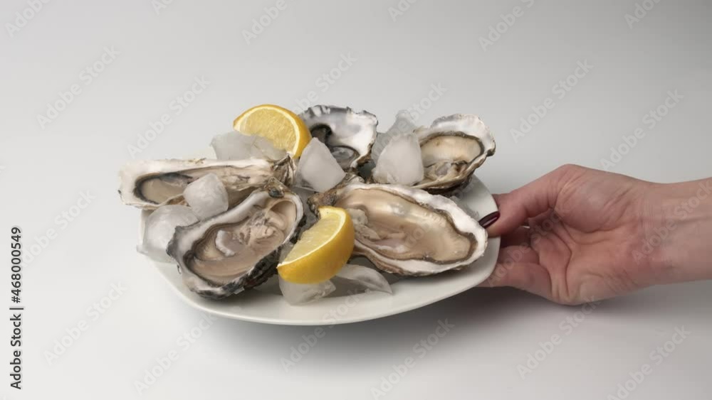Oysters on ice with lemon closeup. Fresh Oyster on half shell on big plate in restaurant. Served table. 4K UHD video slow motion Oysters on ice with lemon closeup. Fresh Oyster on half shell on big plate in restaurant. Served table. 4K UHD video slow motion