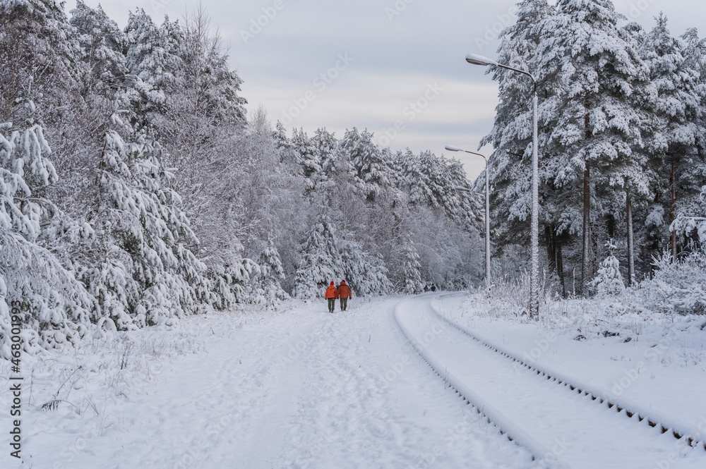 Two unrecognizable people in red jackets walking by the abandoned railway rails in snowy white forest Two unrecognizable people in red jackets walking by the abandoned railway rails in snowy white forest
