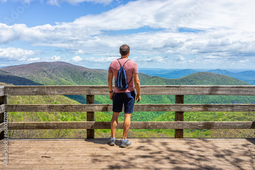 One young man with drawstring bag backpack standing on observation overlook deck wooden platform at Wintergreen ski resort town on nature Highlands leisure hiking trail, Virginia photo