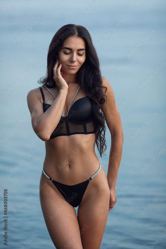 Sexy brunette in a black bikini posing on the beach. High quality photo Sexy brunette in a black bikini posing on the beach. High quality photo