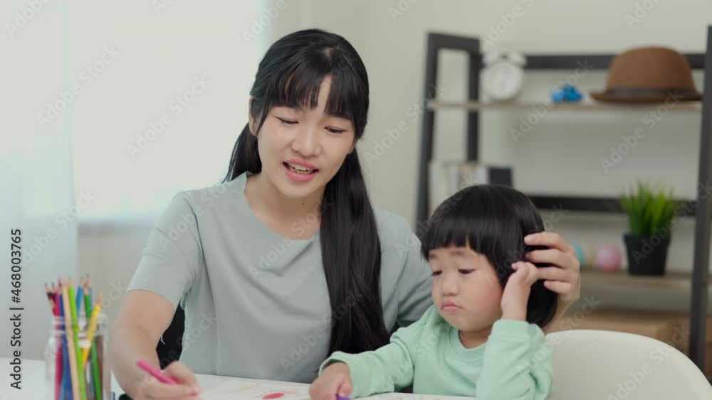 Happy asian boy painting with crayon and colored pencil with his mother in living room at home. Mom teaching son how to painting with crayon color on book or doing homework. family concept.