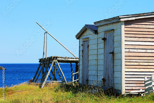 A fishing stage and fishing sheds on a grassy hill, next to the Atlantic Ocean. © Stephen