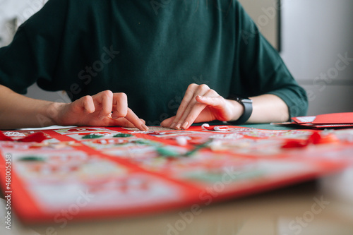 Close-up of unrecognizable young woman gluing envelopes on board with gifts for children making Christmas advent calendar at home, selective focus, blurred background. Preparing for xmas, new year.