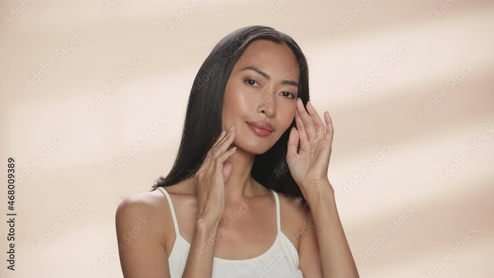Female Beauty Portrait. Beautiful Asian Brunette Woman Posing, Smiling, Touching Her Face with Natural, Healthy Skin. Wellness and Skincare Concept on Soft Isolated Background. Close Up. Female Beauty Portrait. Beautiful Asian Brunette Woman Posing, Smiling, Touching Her Face with Natural, Healthy Skin. Wellness and Skincare Concept on Soft Isolated Background. Close Up.