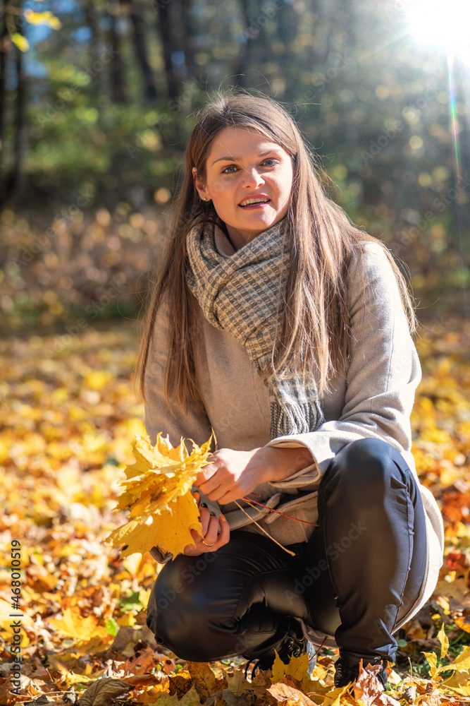 Beautiful brunette woman with bouquet of yellow maple tree leaves enjoy warm and sunny autumn day in park. Bright vivid backlight filter with sun light flare beams