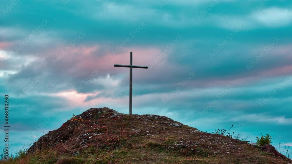 Iron Christian cross on a rocky hill. Colorful clouds in motion at sunset. Iron Christian cross on a rocky hill. Colorful clouds in motion at sunset.