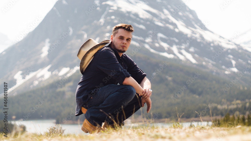 man squatting with cowboy hat in front of a mountain man squatting with cowboy hat in front of a mountain