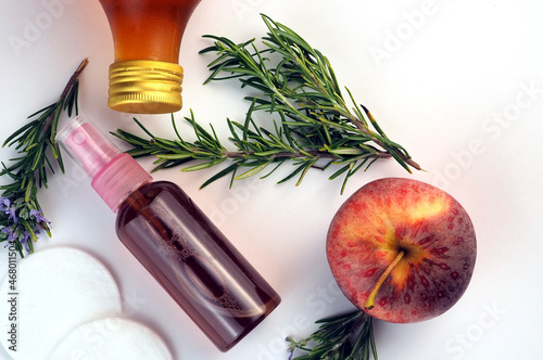 Face toner for acne skin in a bottle, fresh rosemary branches, apple cider vinegar bottle on white background. Flat lay photo