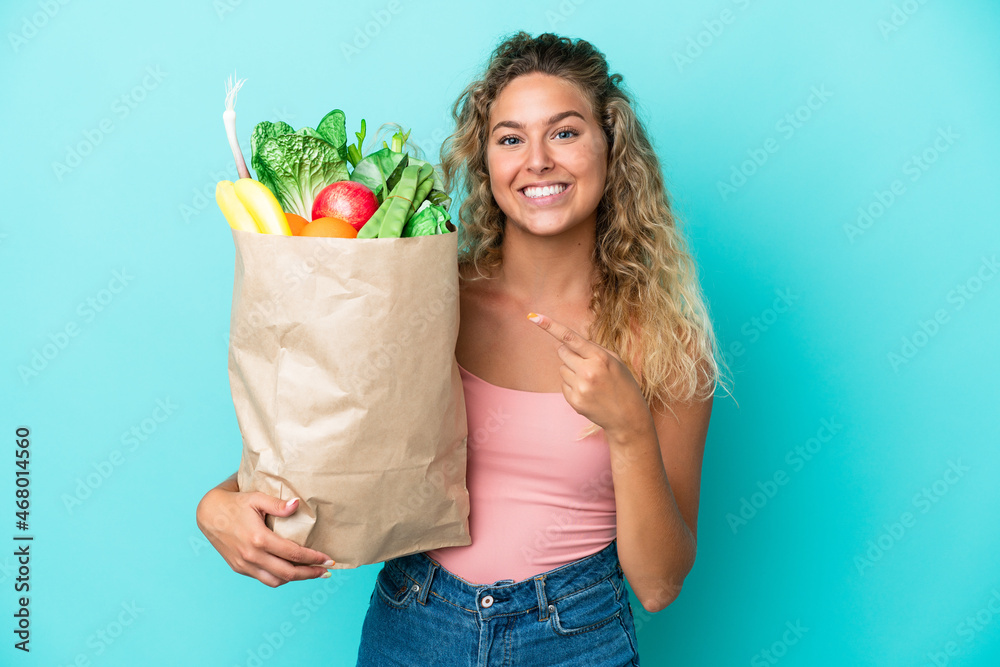 Girl with curly hair holding a grocery shopping bag isolated on green background pointing to the side to present a product Girl with curly hair holding a grocery shopping bag isolated on green background pointing to the side to present a product