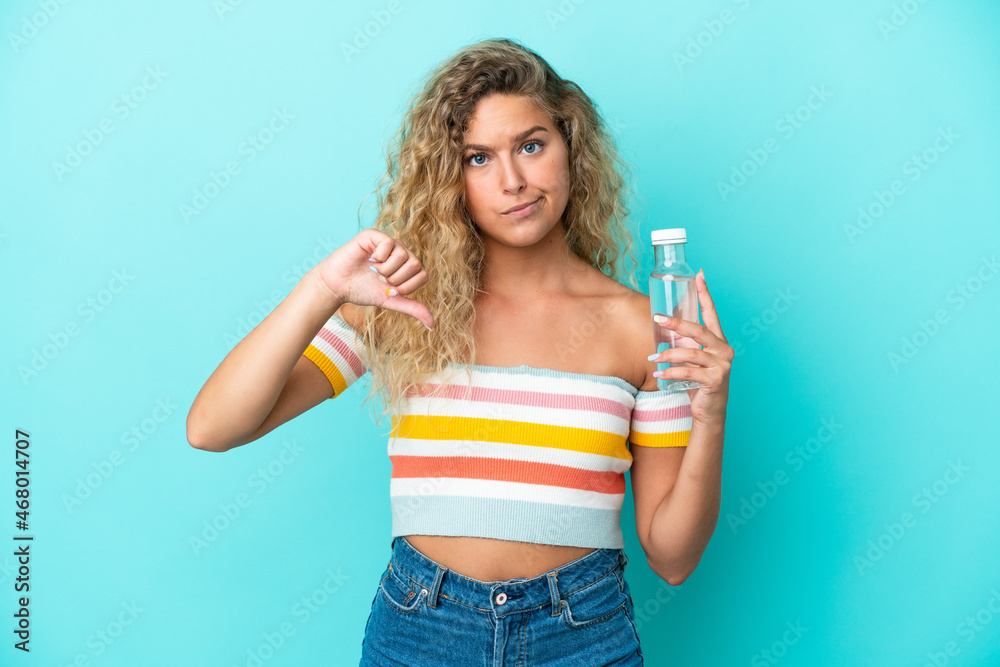 Young blonde woman with a bottle of water isolated on blue background showing thumb down with negative expression Young blonde woman with a bottle of water isolated on blue background showing thumb down with negative expression
