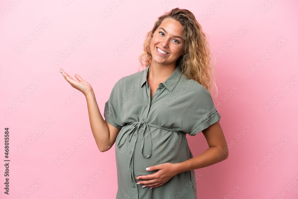 Girl with curly hair isolated on pink background pregnant and presenting something Girl with curly hair isolated on pink background pregnant and presenting something