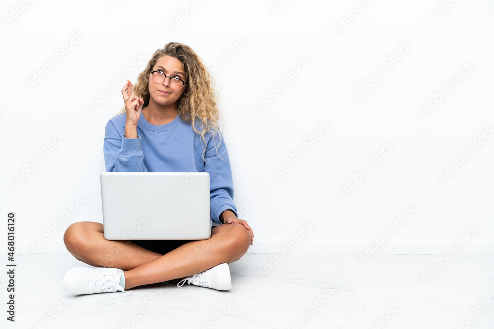 Girl with curly hair with a laptop sitting on the floor with fingers crossing and wishing the best Girl with curly hair with a laptop sitting on the floor with fingers crossing and wishing the best