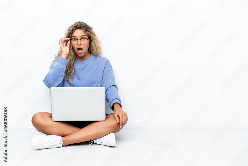 Girl with curly hair with a laptop sitting on the floor with glasses and surprised Girl with curly hair with a laptop sitting on the floor with glasses and surprised