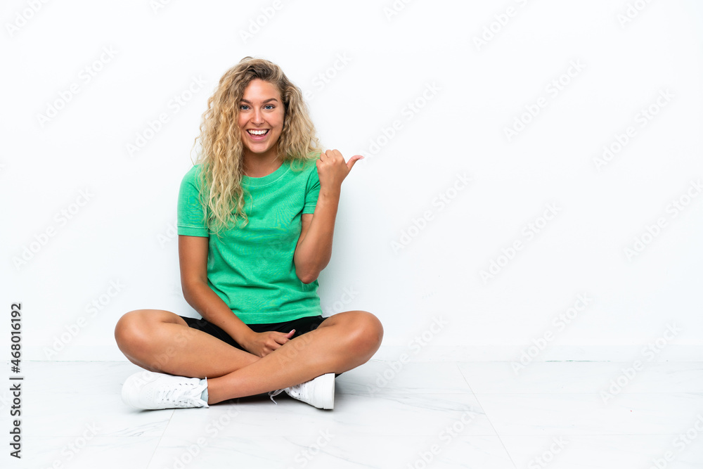 Girl with curly hair sitting on the floor pointing to the side to present a product Girl with curly hair sitting on the floor pointing to the side to present a product