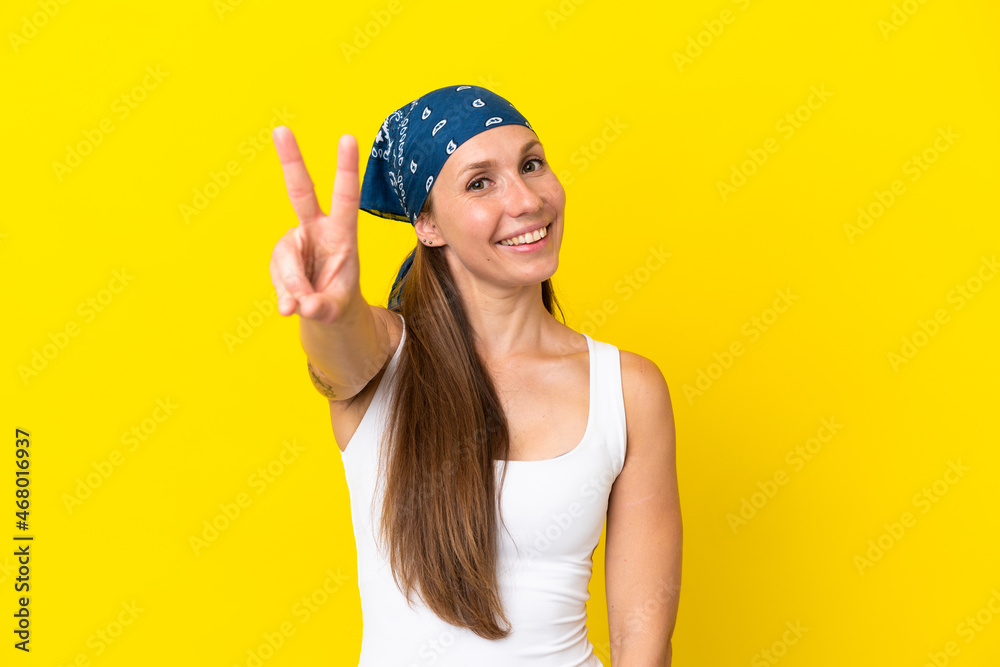 Young English woman isolated on yellow background smiling and showing victory sign Young English woman isolated on yellow background smiling and showing victory sign