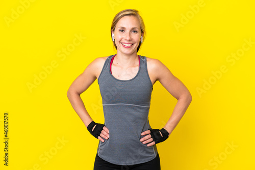 Young English woman isolated on yellow background posing with arms at hip and smiling © luismolinero