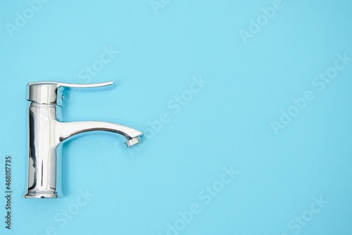 Single handle water tap on light blue background. New chrome or steel mixer tap .